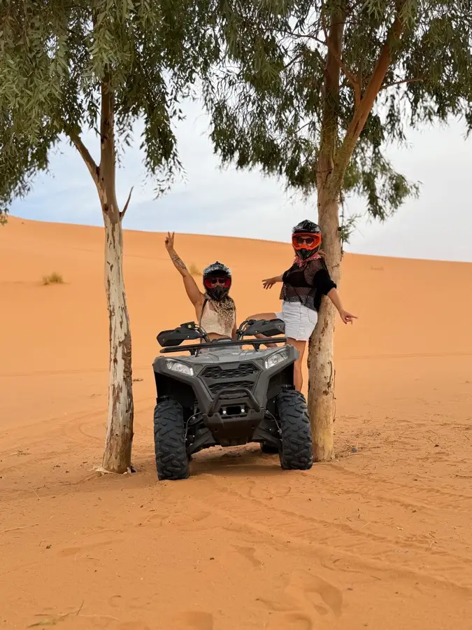Two riders on a quad bike between trees in the Merzouga dunes
