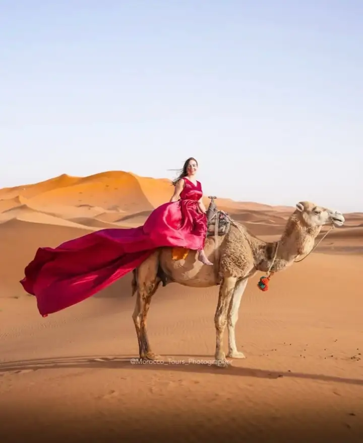 Woman in a red dress riding a camel in the Erg Chebbi dunes