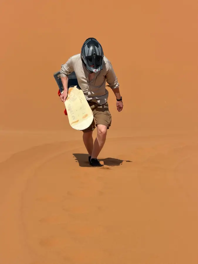 Guide carrying a sandboard across the Erg Chebbi dunes