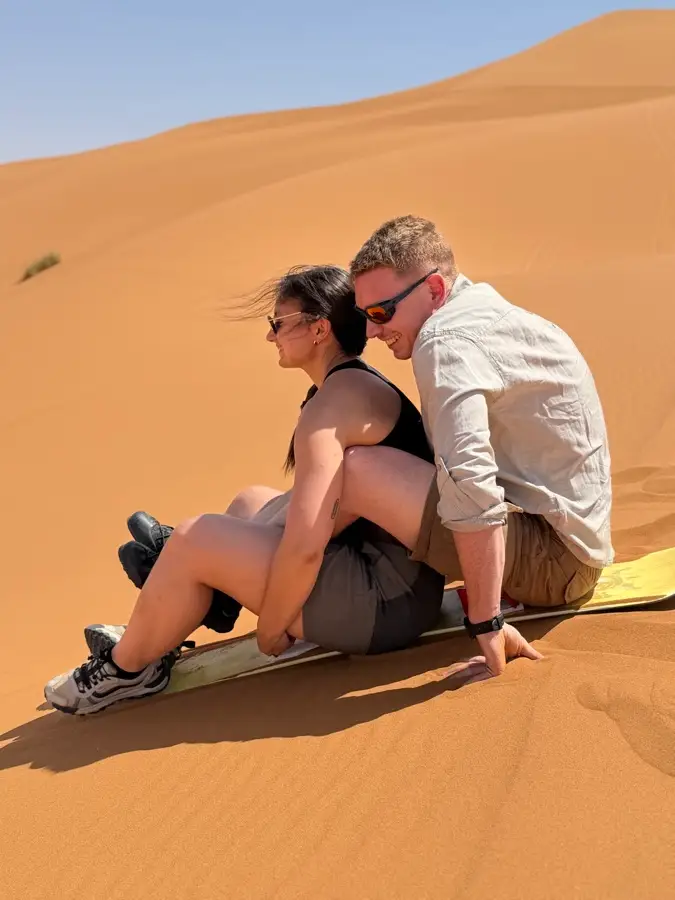 Couple sitting on a sandboard on the dunes of Merzouga